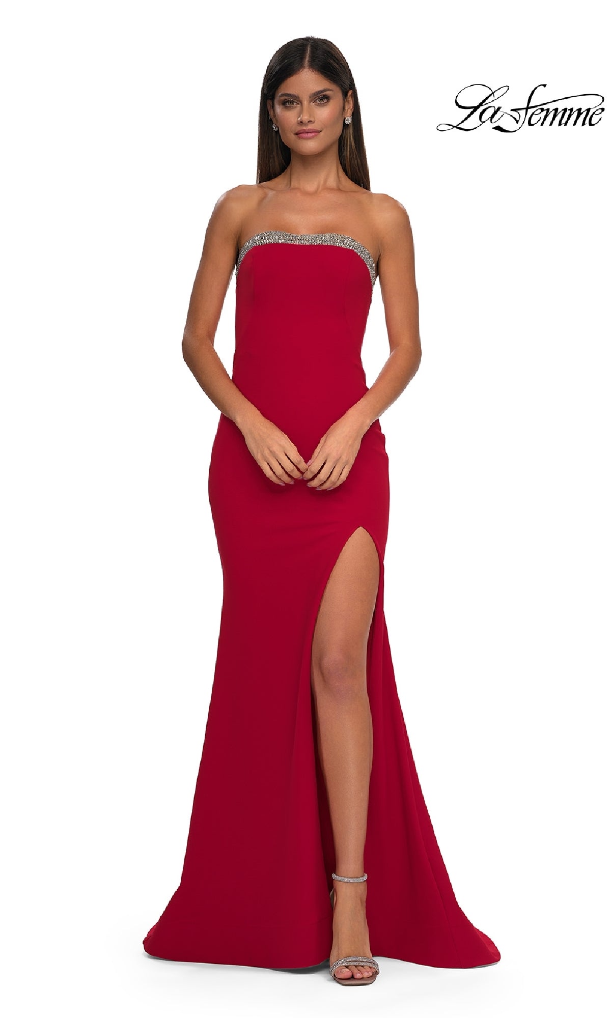 A woman wearing a red Bead-Trimmed Long Prom Dress: La Femme 32891 with a thigh-high slit and silver trim at the top, paired with silver high-heeled sandals, stands against a plain white background.